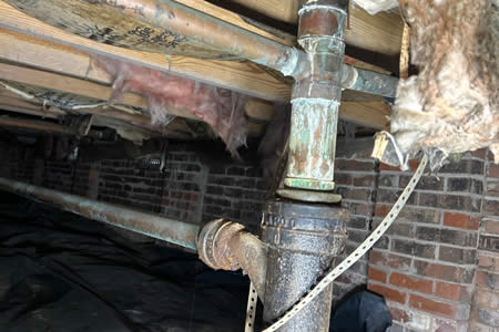 Hard water mineral buildup and corrosion on residential plumbing pipes in a crawl space